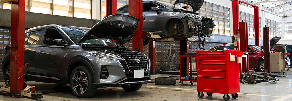 Interior view of a car service and body repair center. With 2 vehicles being worked on within the facility.