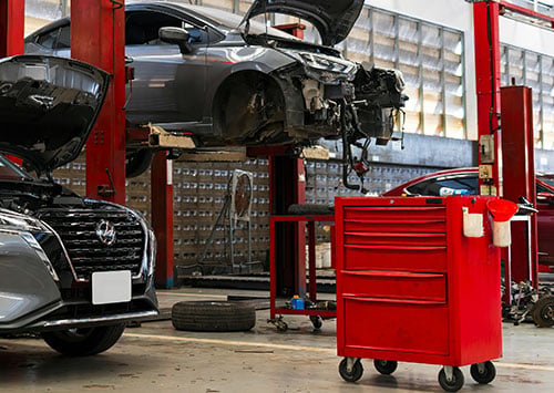 Interior view of a car service and body repair center. With 2 vehicles being worked on within the facility.