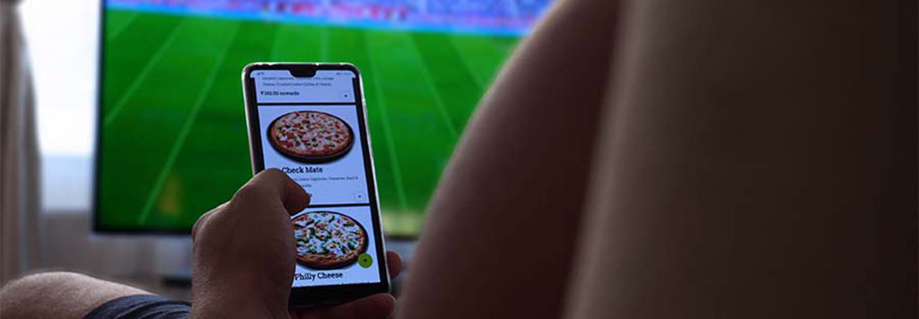 man using pizza delivery app while watching football game on television