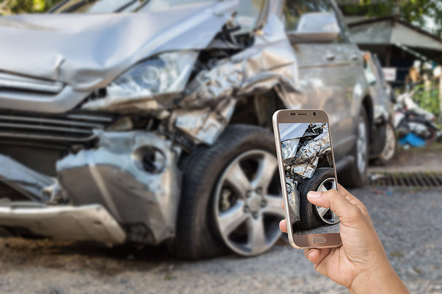 Person holding a mobile phone taking a photo of vehicle damages.