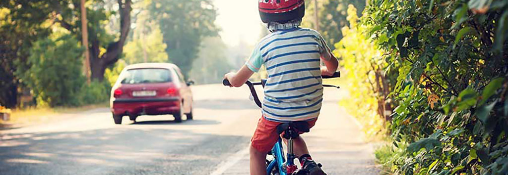 small boy riding a bicycle on the shoulder of a road; car driving by