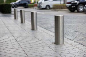 Image of metal bollards built into a sidewalk of a business parking lot, to protect the sidewalk and building.