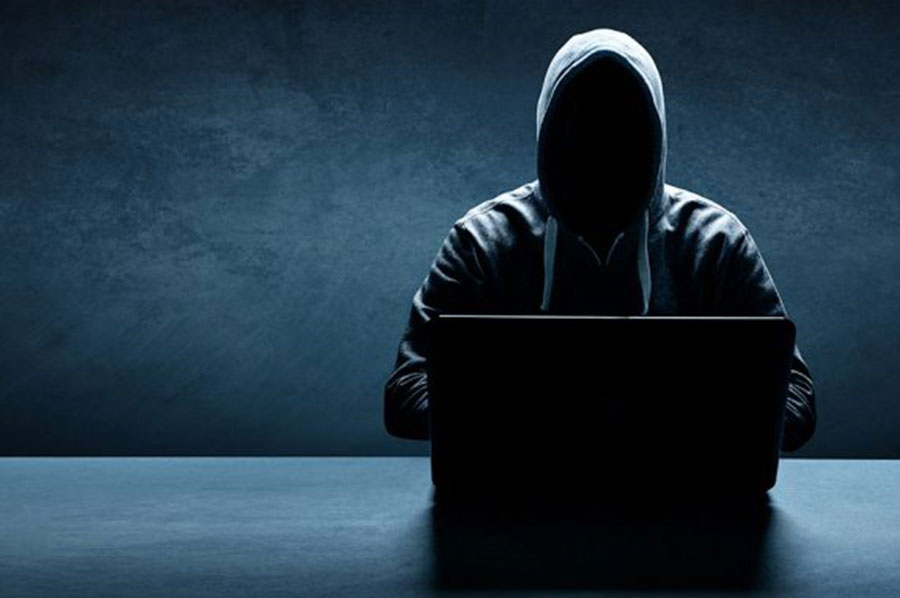 Image of a hooded figure at a table with a computer.