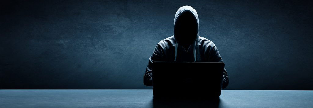 Shadowed man in hoodie typing on a laptop