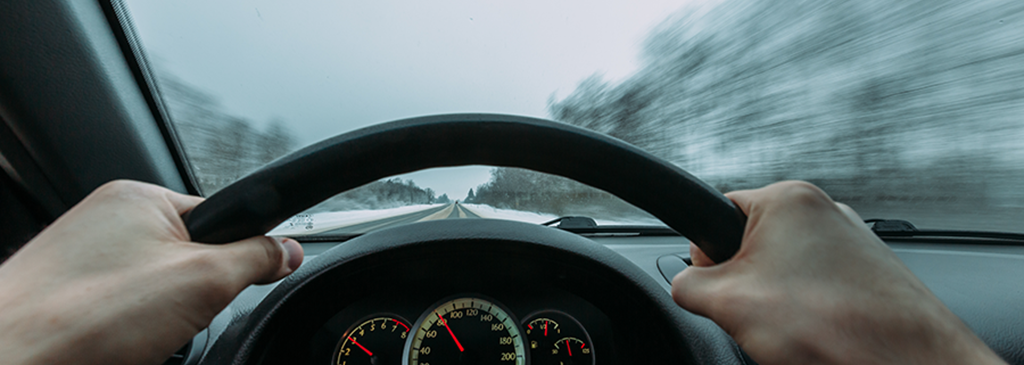 Hands on a steering wheel. Man driving down snowy road