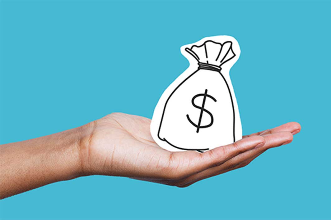 A person's hand holding a black and white bag of money, in front of a light blue background. Hand-delivering savings.