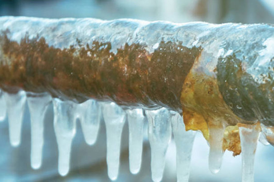 View of a frozen pipe with icicles hanging off of it due to rain and a winter storm.